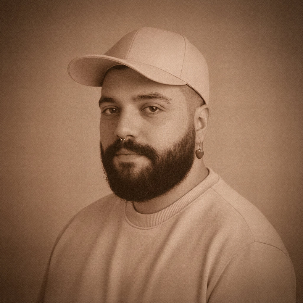 A man, Mohamad Kaaki, with a beard and nose ring wearing a pink baseball cap and a pink crewneck sweatshirt, set against a solid pink background.